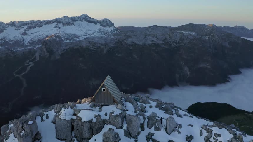 Small grey cabin on the top of a snowy mountain peak