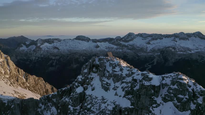 Snowy mountain peaks with a cabin on a summit at sunrise