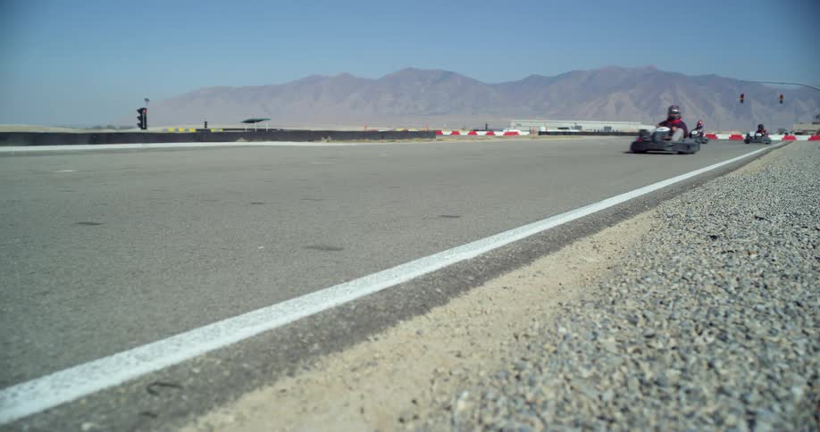 People ride on go karts on a race track outdoors in the daylight with mountains in the background