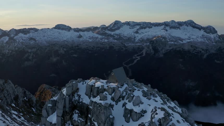 A lone building on the snowy peak of a mountain in the evening