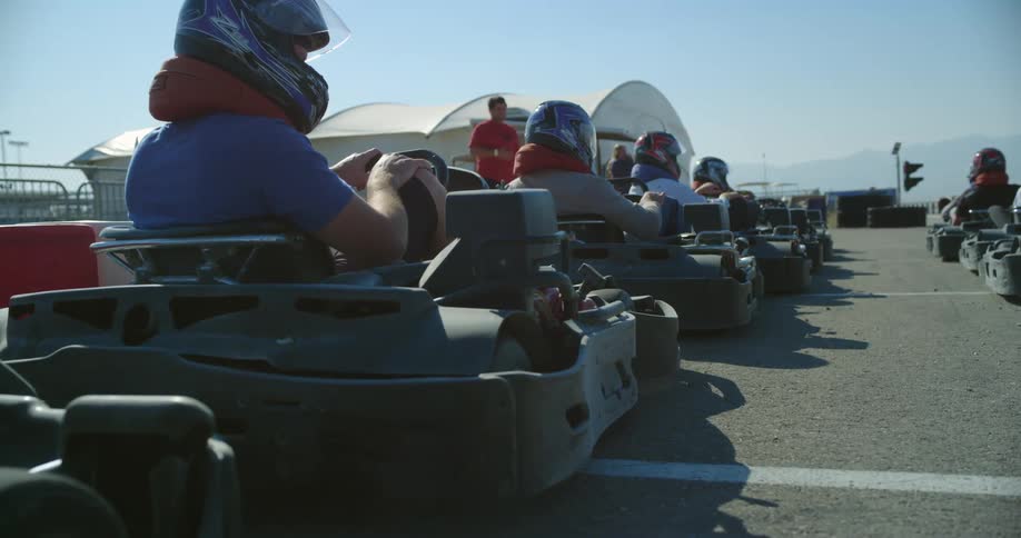 Men wear helmets as they sit in a line of go karts in a parking lot