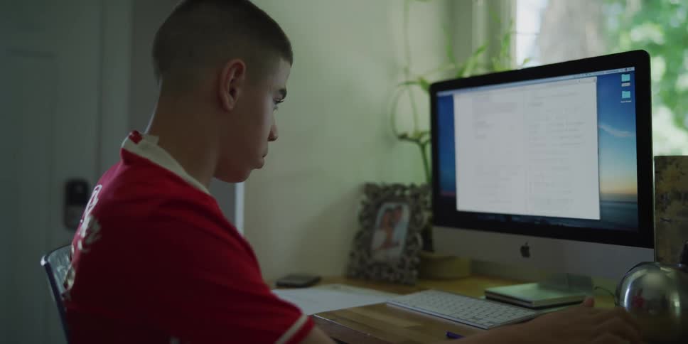 Boy at home sitting in front of a desktop computer scrolling down on a page