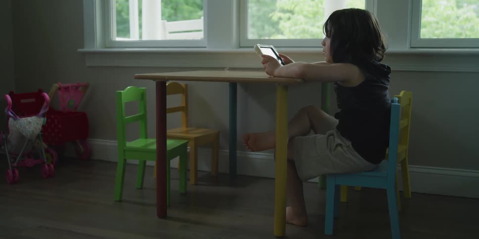 Little boy sitting at a small kids table at home using a tablet