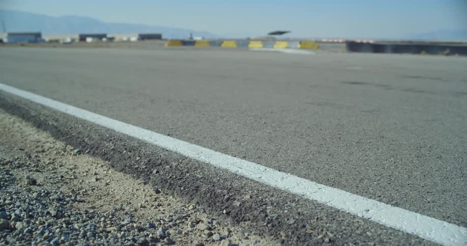 A close up of an asphalt race track with go karts moving down the track quickly