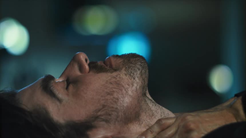 A man laying down then sitting up with lights in the background