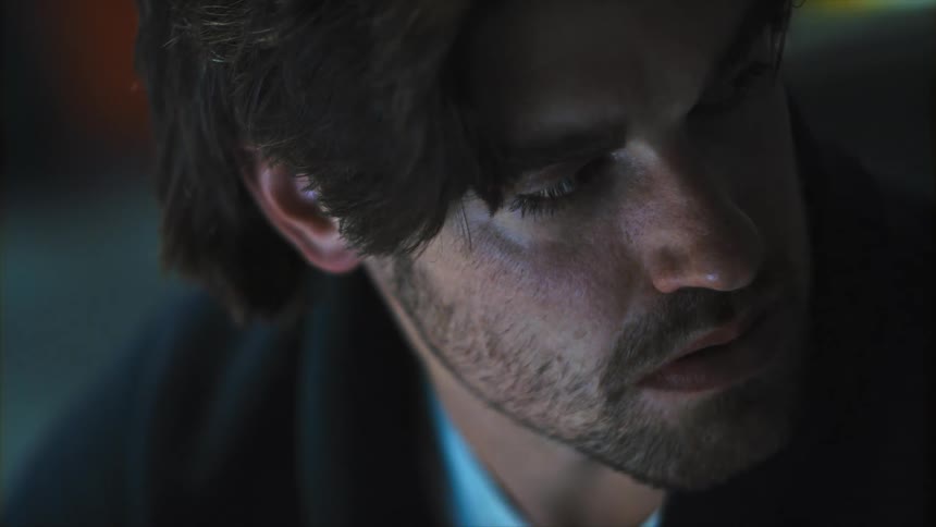 Close up of a young bearded mans face in a dimly lit room