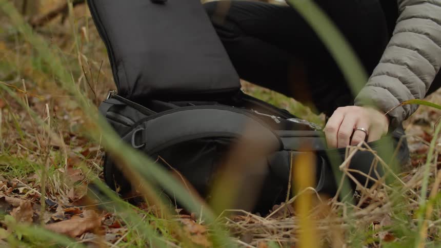 Man opening a black backpack on the ground in a forest