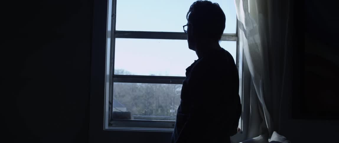 Silhouette of a man standing in a room looking out of a window