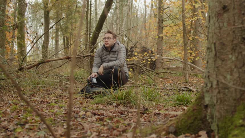Man squatting down picking up a camera out of a bag in a forest