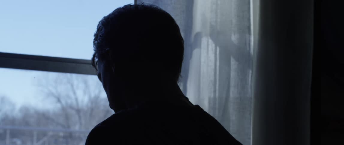 Man from behind taking off his glasses standing in front of a window looking down