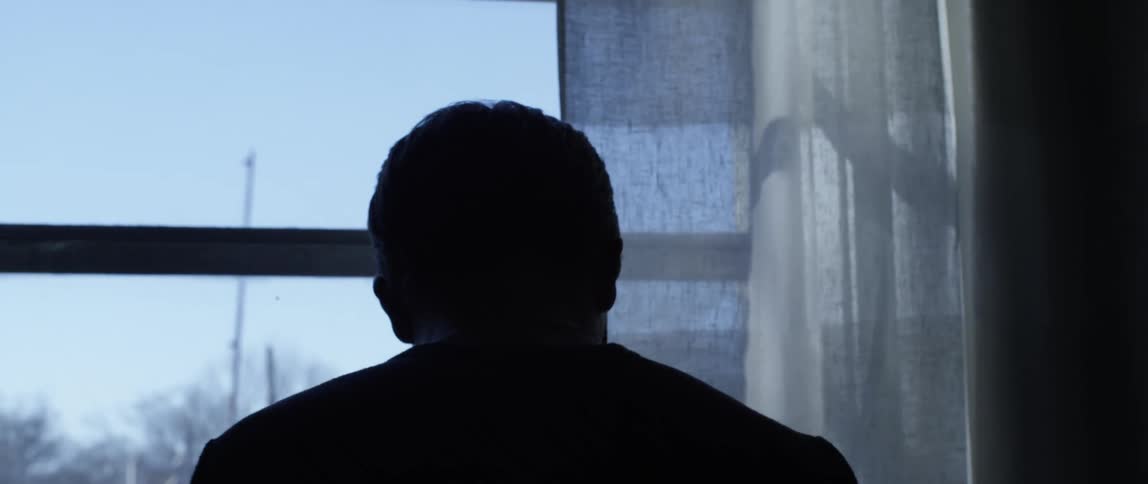 A man lowers his head in sadness and turns away from a window