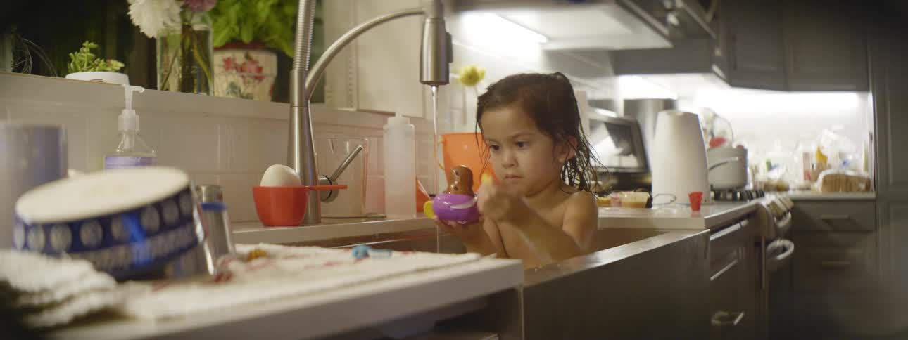 A little girl bating in a kitchen sink and playing with toys