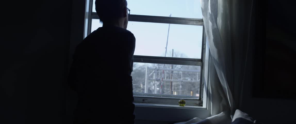 Silhouette of a person inside a dark room looking outside through a window