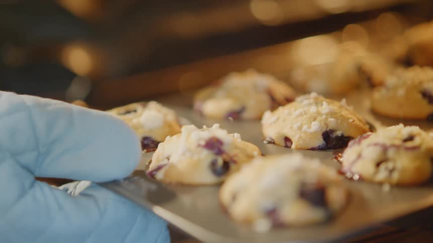 Someone wearing oven mitts removes a tray of muffins from an oven