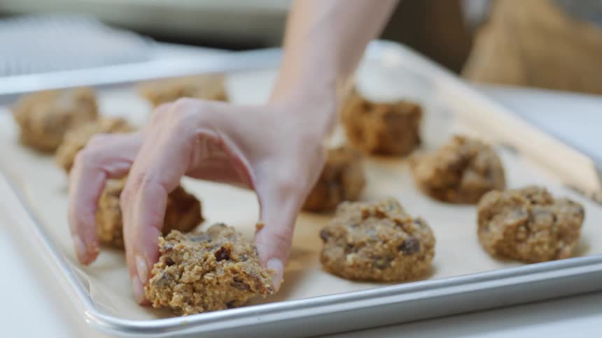 A person places raw cookies on a baking sheet