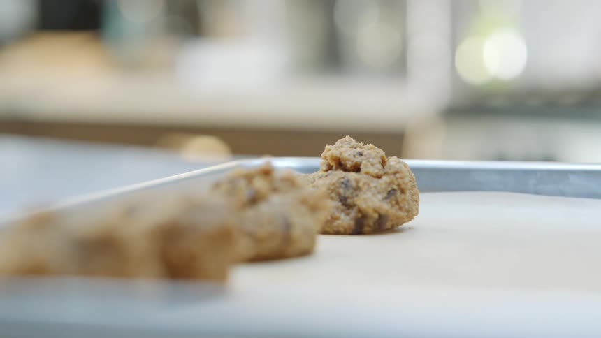 A person placing cookie dough over baking paper in a metal tray on a kitchen