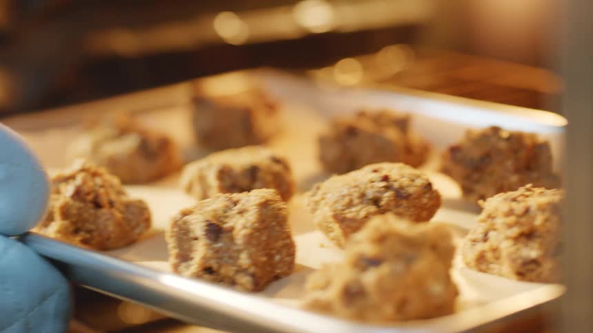 A woman placing a tray of raw cookies inside an oven at home