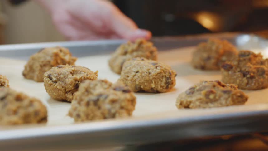 A woman places a baking sheet lined with parchment paper and cookies into an oven