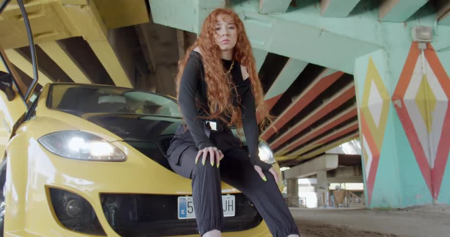 A woman sitting in front of a car with the headlights on and the doors open