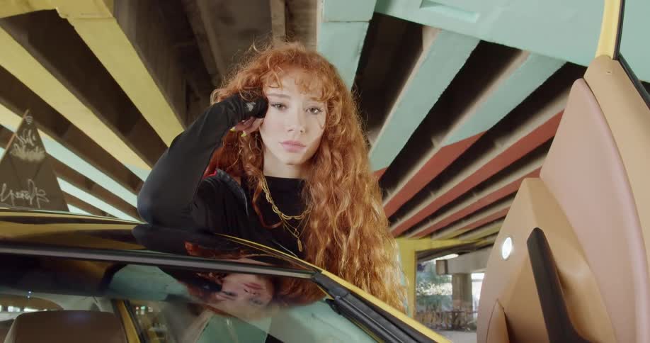 A red headed woman standing next to a luxury sports car