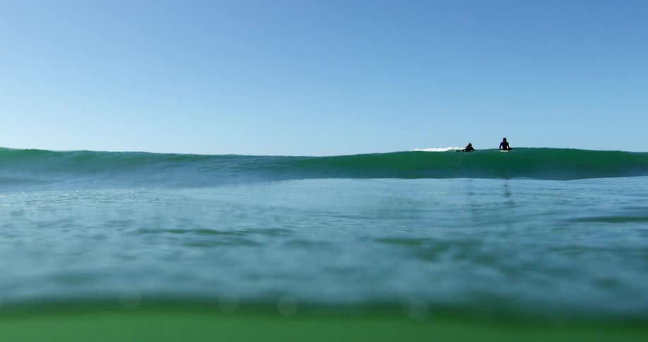 Ocean water rising up and down while two people swim in the distance at daytime