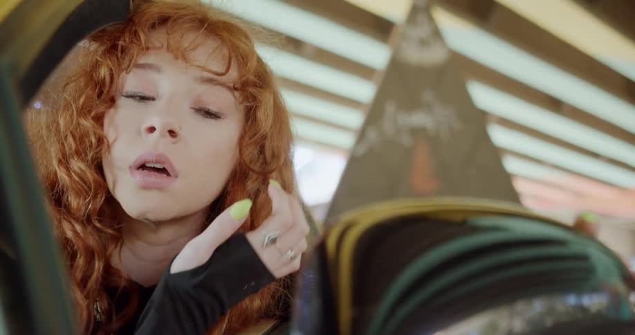 Young redheaded woman looks at herself on the rearview mirror on a car