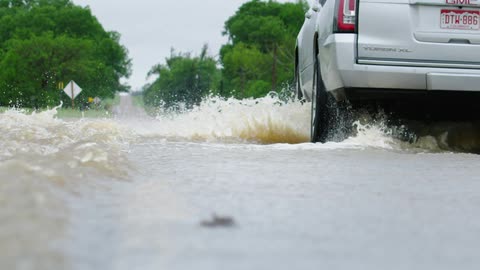 Slow motion shot of a white SUV driving across a flooded roadway during heave afternoon thunderstorms and spring floods in rural America