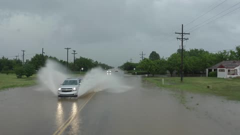 Aerial shot of a car spraying water high into the skay on a flooded highway in rural America