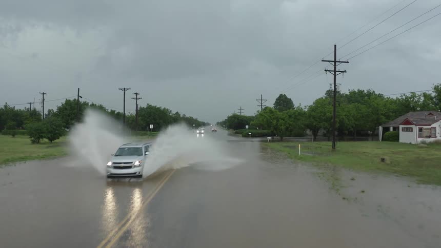 Aerial shot of a car spraying water high into the skay on a flooded highway in rural America