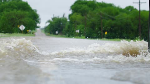 A flooded roadway is seen in this slow motion shot as an SUV forges the waterway and splashes water across the road