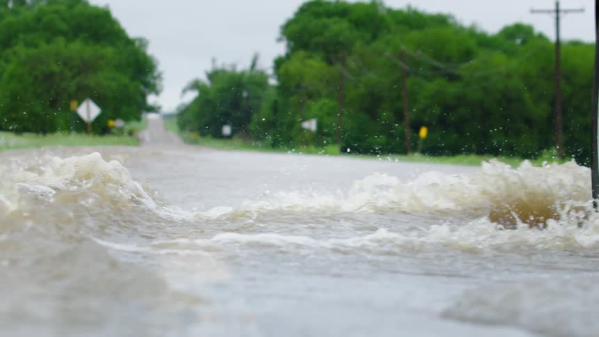 A flooded roadway is seen in this slow motion shot as an SUV forges the waterway and splashes water across the road