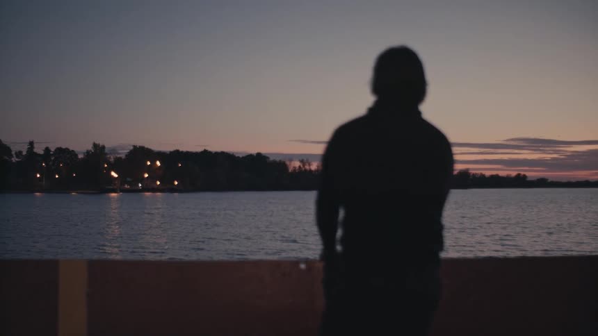 Silhouette of a person looking at a coastal town from a barge at sunset