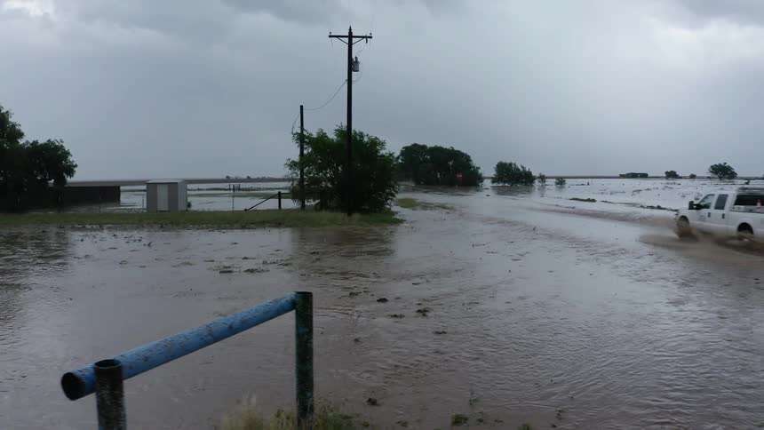 Aerial dolly shot of a white emergency vehicle driving through flooded rural farmland as the utility worker inspected damaged equipment