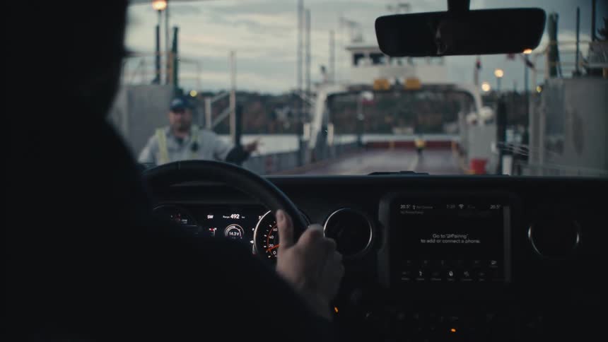 Man drives a vehicle onto a transport ferry parked at a dock