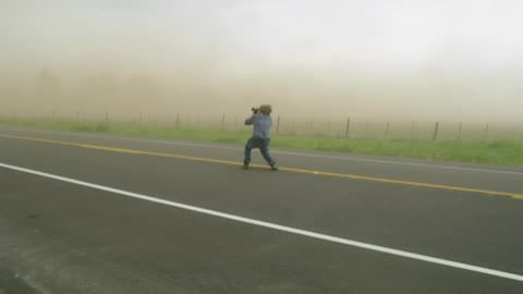 A man gets low to stay balanced as he photographs intense storm winds during a very strong severe thunderstorm