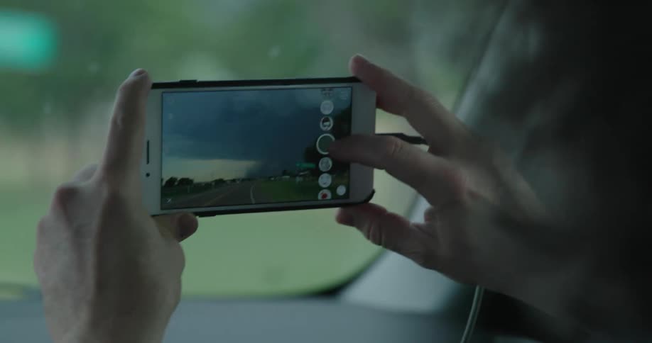 A man in a vehicle taking a picture with a smart phone with a severe thunderstorm weather event in the photo