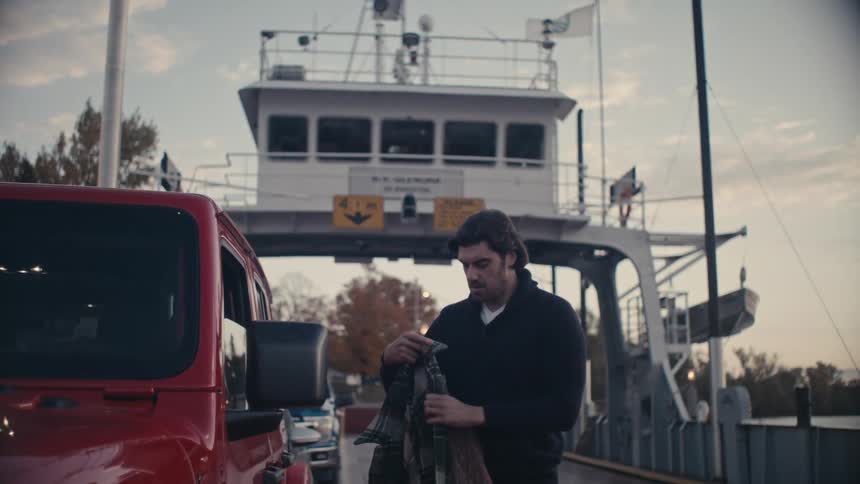 A man steps out of his vehicle parked on a ferry and puts his coat on