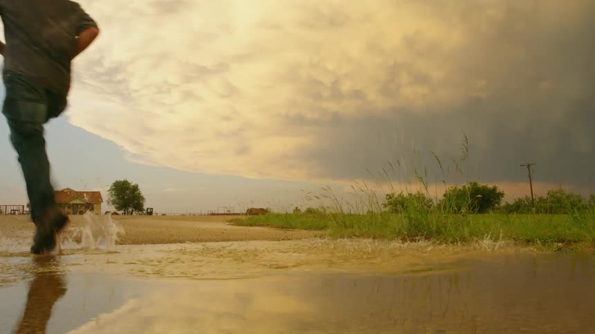 Reflection shot showing a huge thunderstorm being illuminated by the setting sun just before a man leaps across the puddle and creates a big splash