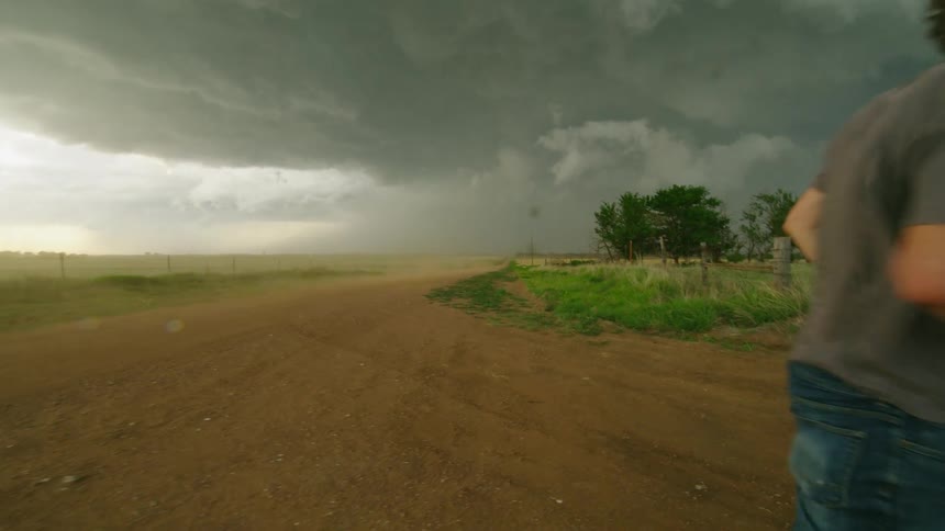Photographer man walks back to his car as a huge dust plume barrels towards the storm chasers on a dusty road in Middle Ameica
