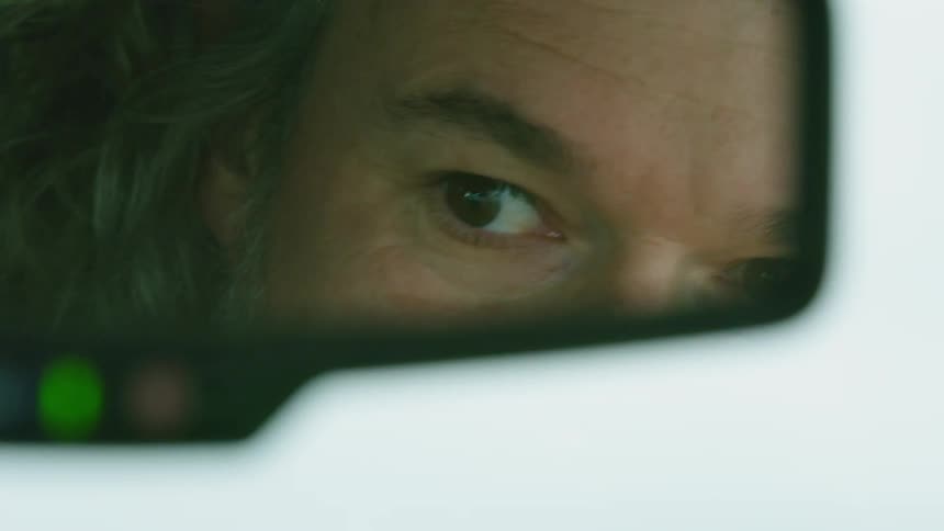 Tight shot of a rugged and adventurous man as he scans the horizon for tornados in the reflection of the rear view mirror