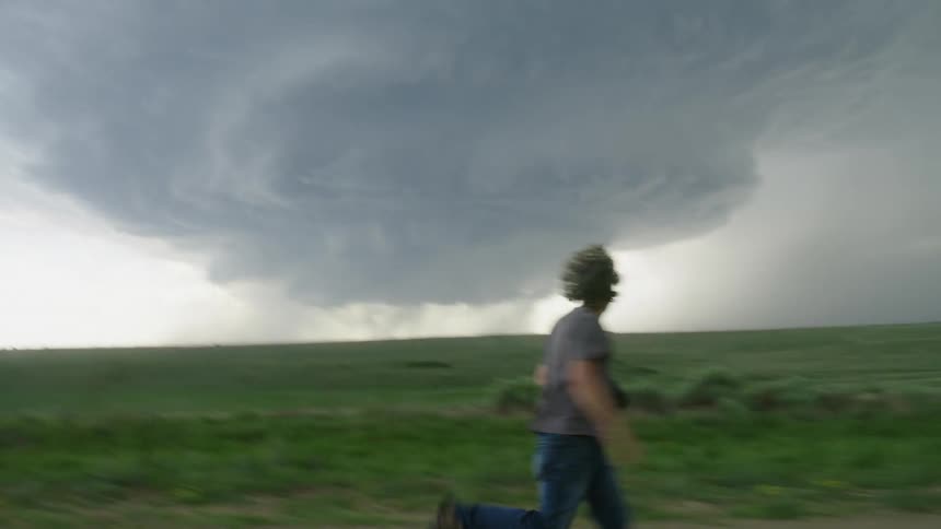 A man runs fearfully on a dirt rural road looking behind just after a huge bolt of lightning struck nearby, there is a massive storm system in the background