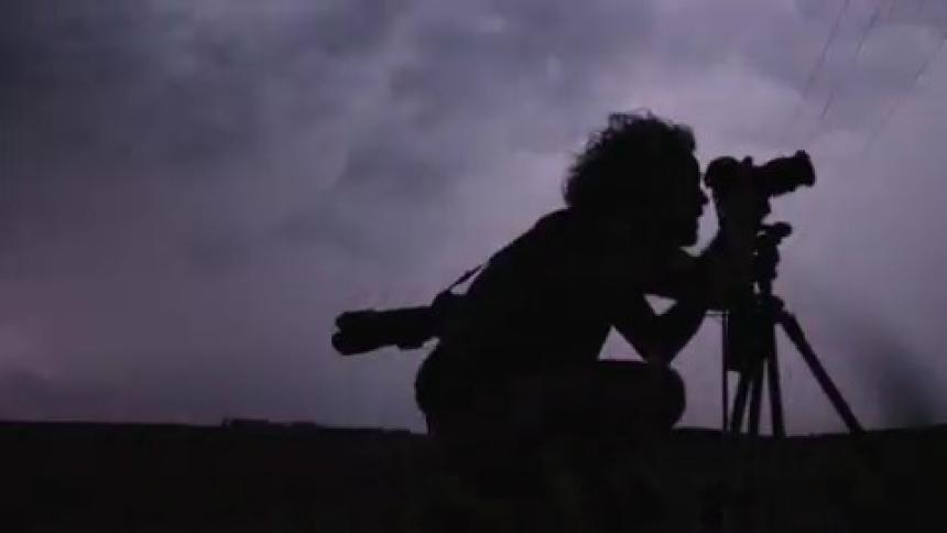 Silhouette of a man taking pictures at night being illuminated by huge lightning strikes behind him revealing the chaotic scene and intense storm clouds behind him