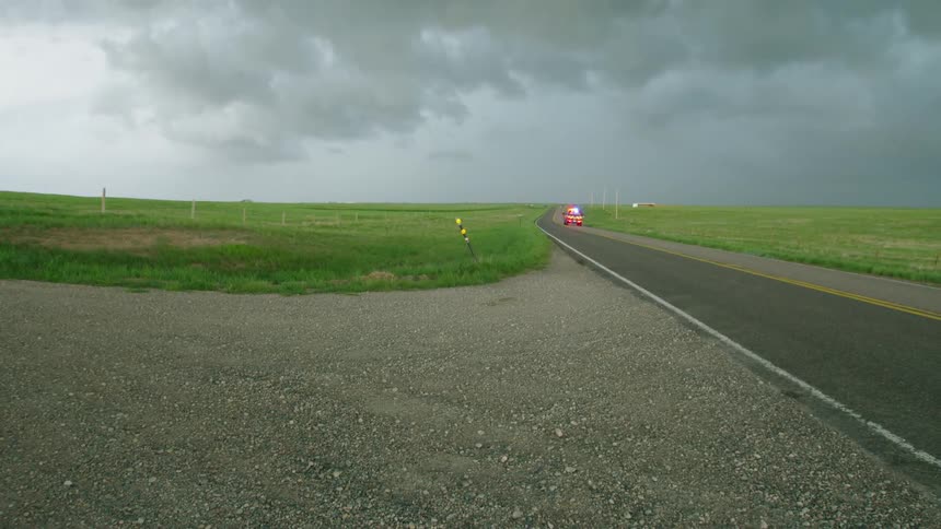 An emergency vehicle with the sirens on rushes by a photographer after a tornado struck a small Wyoming town in late May tornado season