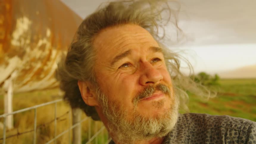 A rugged and handsome adventurous middle aged man looks over his shoulder at a supercell thunderstorm over the horizon in golden evening light