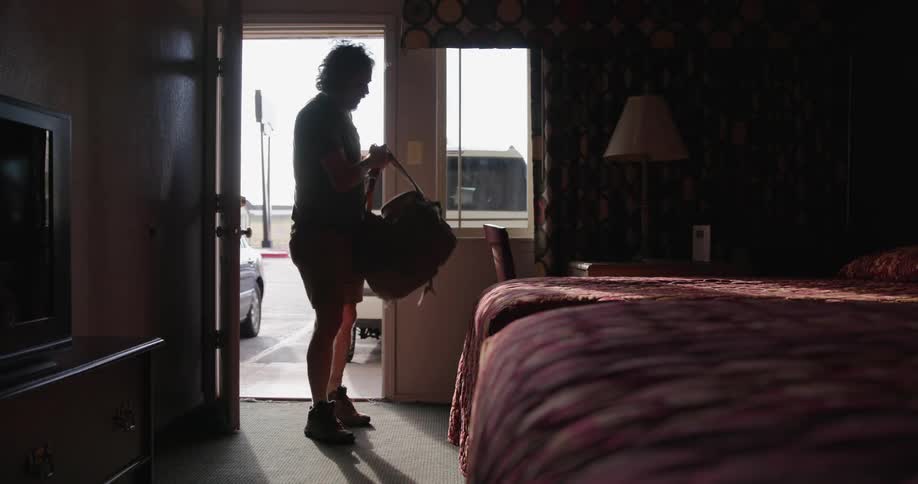 A storm chaser man checks into a dingy motel and lays down exhausted on the bed after pushing it on the road all day in chasing severe weather