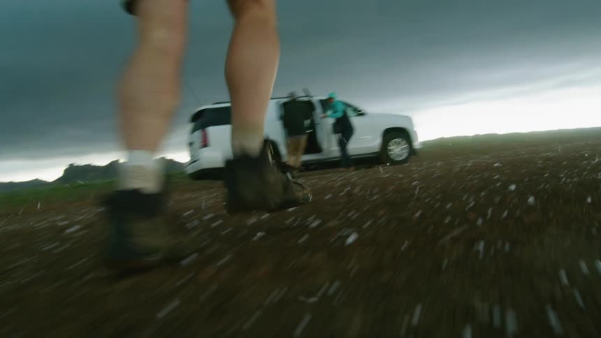 Hail stones pound down around a man as he runs quickly towards the shelter of a car during a severe weather hail storm