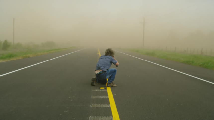 An adventurous middle aged man photographs a massive thunderstorm super cell event as hurricane force winds blow his hair and dust everywhere