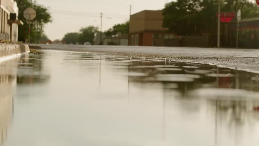 Real time static shot of rain drops falling into a puddle that's formed on the side of a street in small town Texas, USA