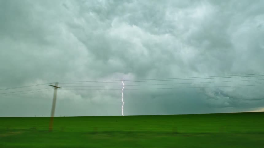 Strong Cloud to Ground lightning flashes in dark and ominous severe weather storm clouds in this moving vehicle shot
