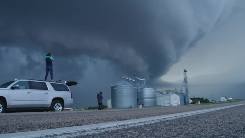 Woman standing on top of an SUV filming a mothership supercell cloud weather event while bucket list storm chasing